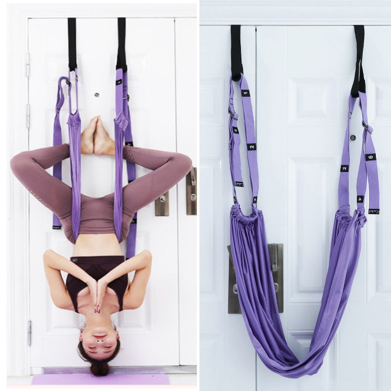 A person using a purple yoga inversion and stretching strap to assist with a yoga pose, hanging from a door frame.