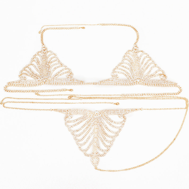 A woman wearing a gold-colored body chain that connects to a bra and panties, laid out on a bed.