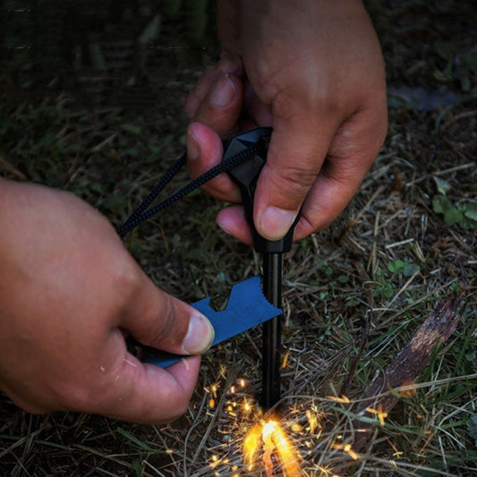 A person's hands using a black multifunctional flint tool to create sparks on a wooden surface.