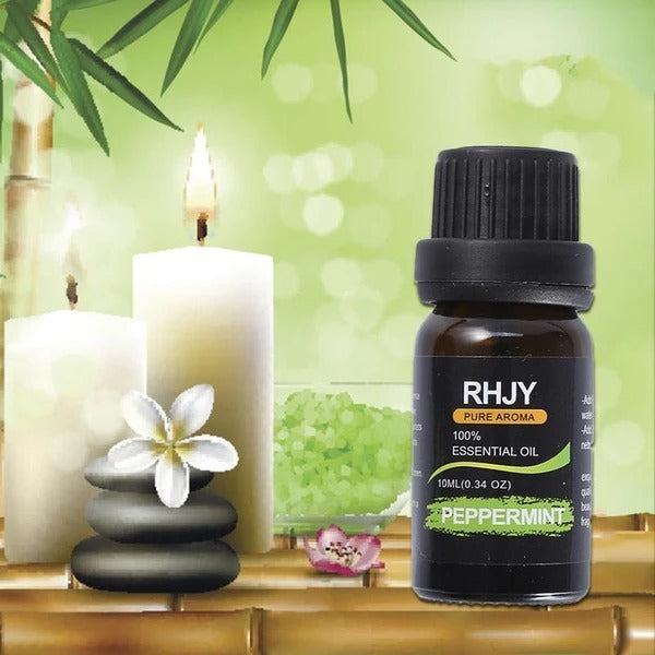 Bottle of peppermint essential oil with candles and flowers on a bamboo surface.