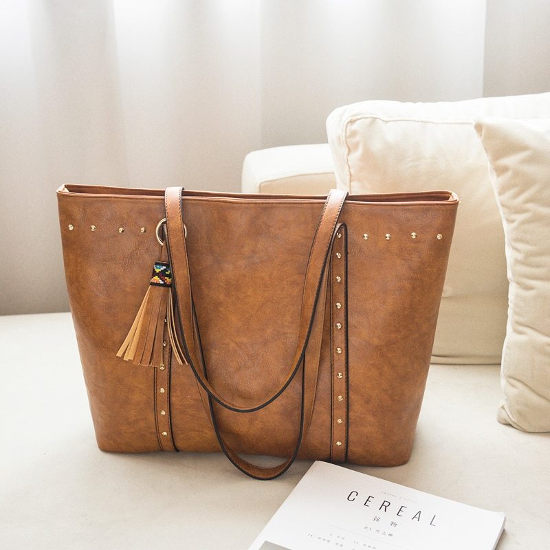 A brown faux leather shoulder crossbody bag with a tassel detail on a sofa.
