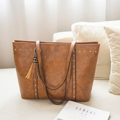 A brown faux leather shoulder crossbody bag with a tassel detail on a sofa.