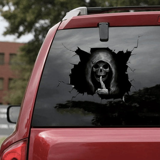 A black skull car decal sticker applied on the rear window of a red car, creating a 3D illusion of the skull breaking through the glass.