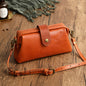 A brown leather purse with a cover type opening, a shoulder strap, and a front flap with a metal snap button.