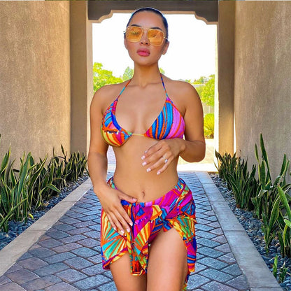 Woman in colorful bikini and sarong on a pathway with plants on either side.