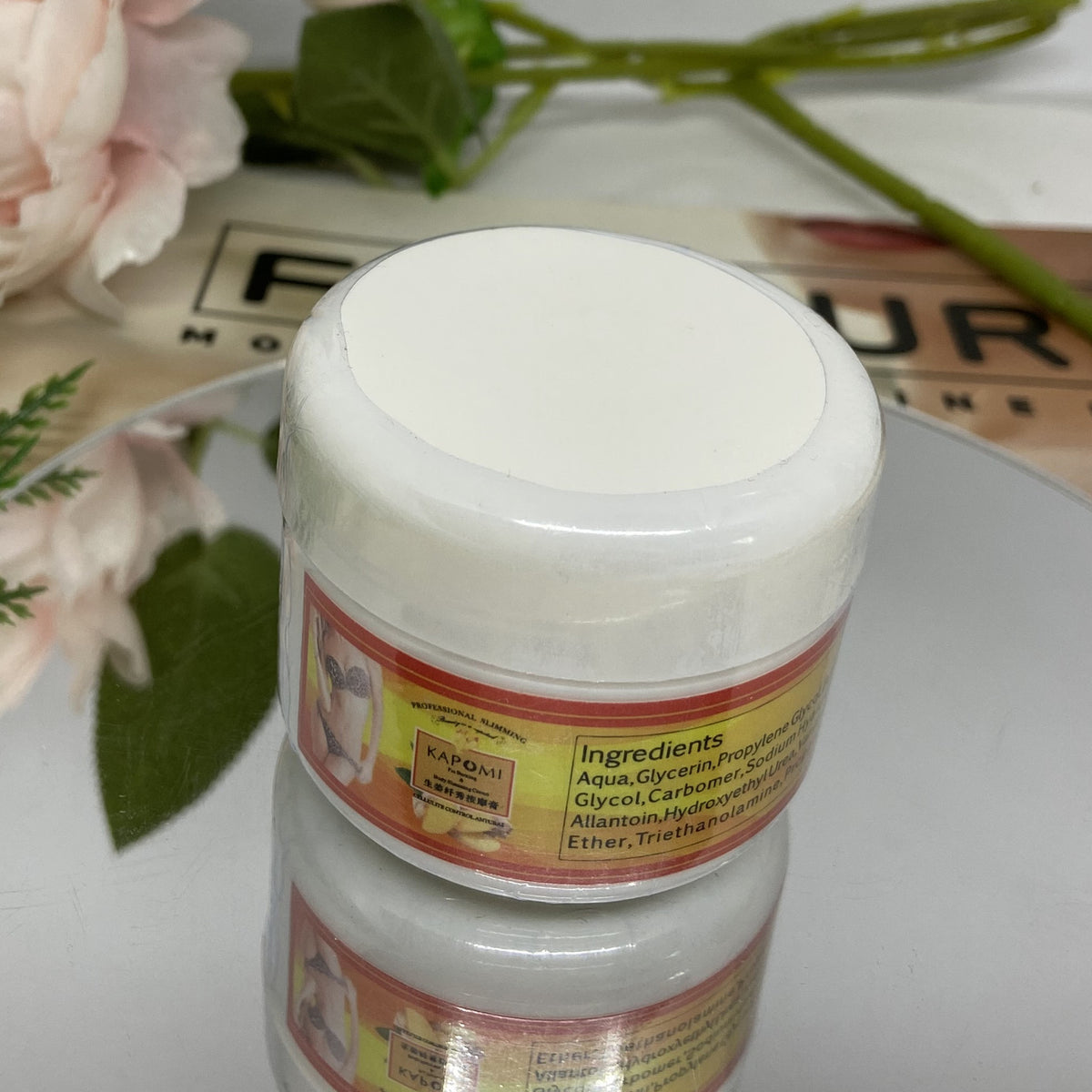 An advertisement image showing a container of KAPOMI body slimming cream with a yellow label. In the background, a person is measuring their waist with a measuring tape.