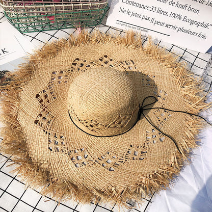 A beige raffia straw hat with a wide brim and a black ribbon, displayed on a flat surface.