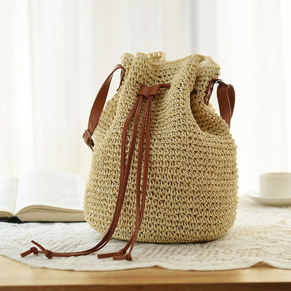 A beige ethnic style drawstring woven straw bag with a polyester texture, displayed on a table with a soft background.