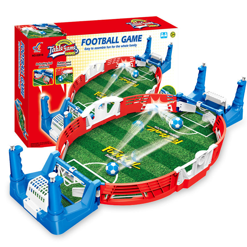Mini tabletop soccer game kit with a red and blue plastic board, green playing field, and white and red soccer balls. The product is packaged in a color box shown in the background.