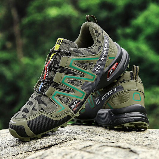 A pair of green camouflage hiking shoes placed on a rock with greenery in the background.