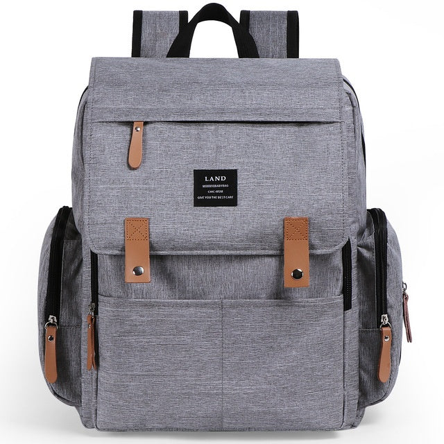 A gray diaper backpack with brown leather accents and multiple compartments, featuring a brand label that reads 'LAND'. The backpack includes shoulder straps and a handbag strap.
