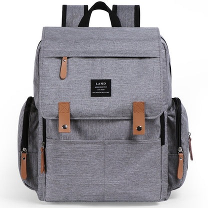 A gray diaper backpack with brown leather accents and multiple compartments, featuring a brand label that reads 'LAND'. The backpack includes shoulder straps and a handbag strap.