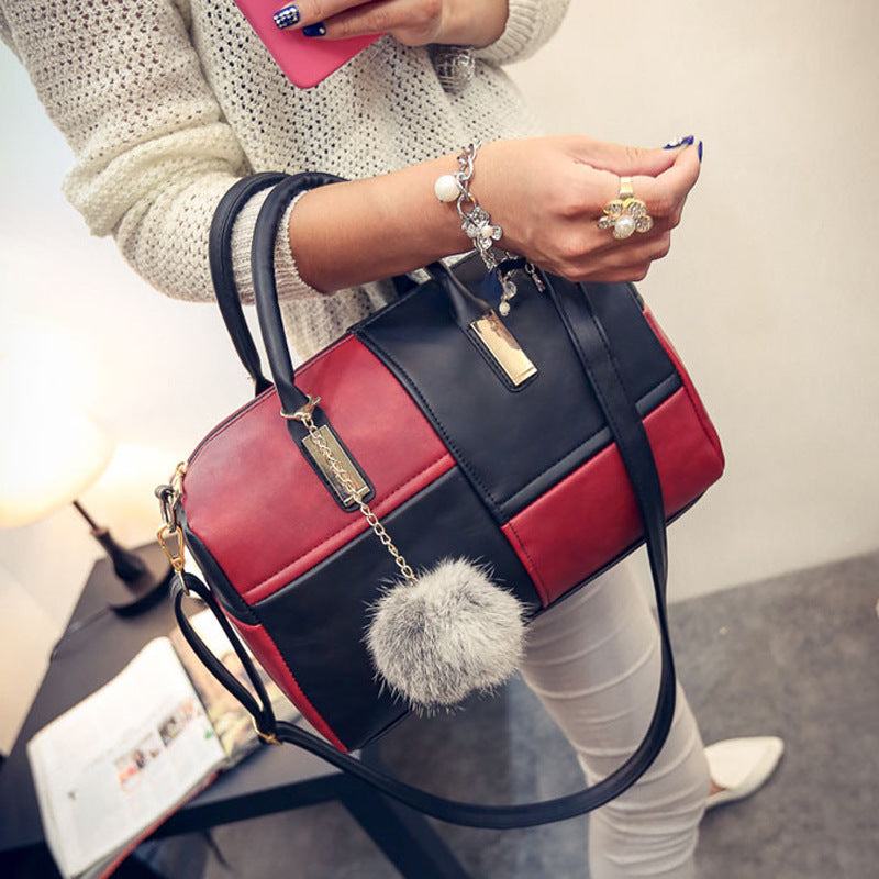 A woman holding a red and black handbag with a grey faux fur pom-pom attached to it.