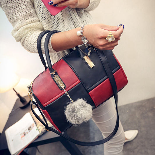 A woman holding a red and black handbag with a grey faux fur pom-pom attached to it.