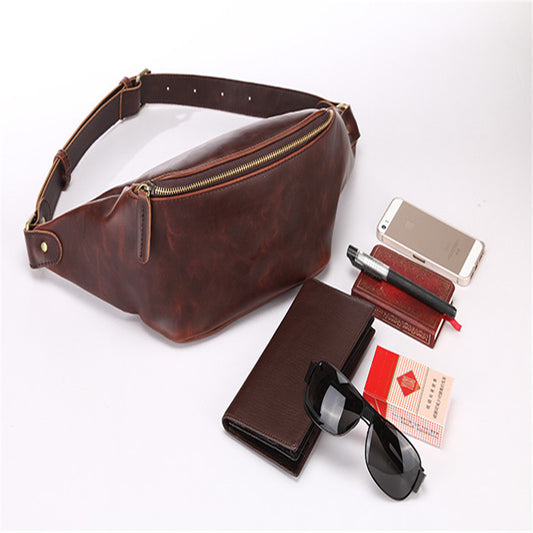 A brown retro men's waist bag made from Crazy Horse PU Leather, displayed alongside accessories such as sunglasses, a notebook, and a smartphone.