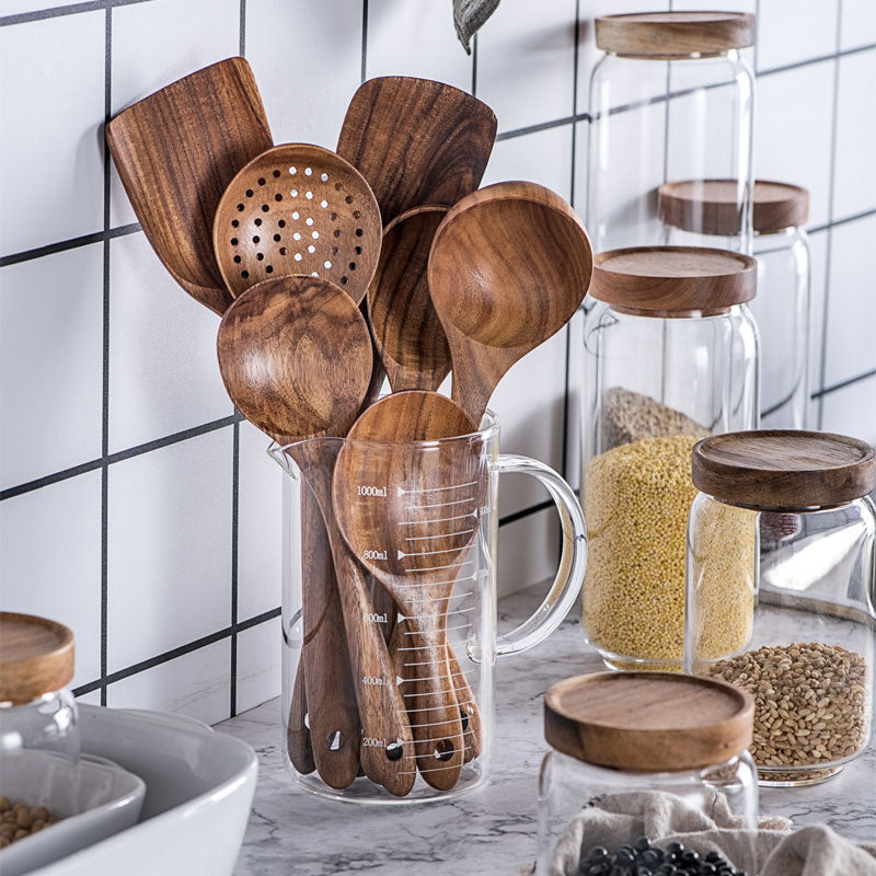 A set of wooden kitchen utensils including a ladle, spoon, turner, and colander, displayed in a clear container on a kitchen counter.