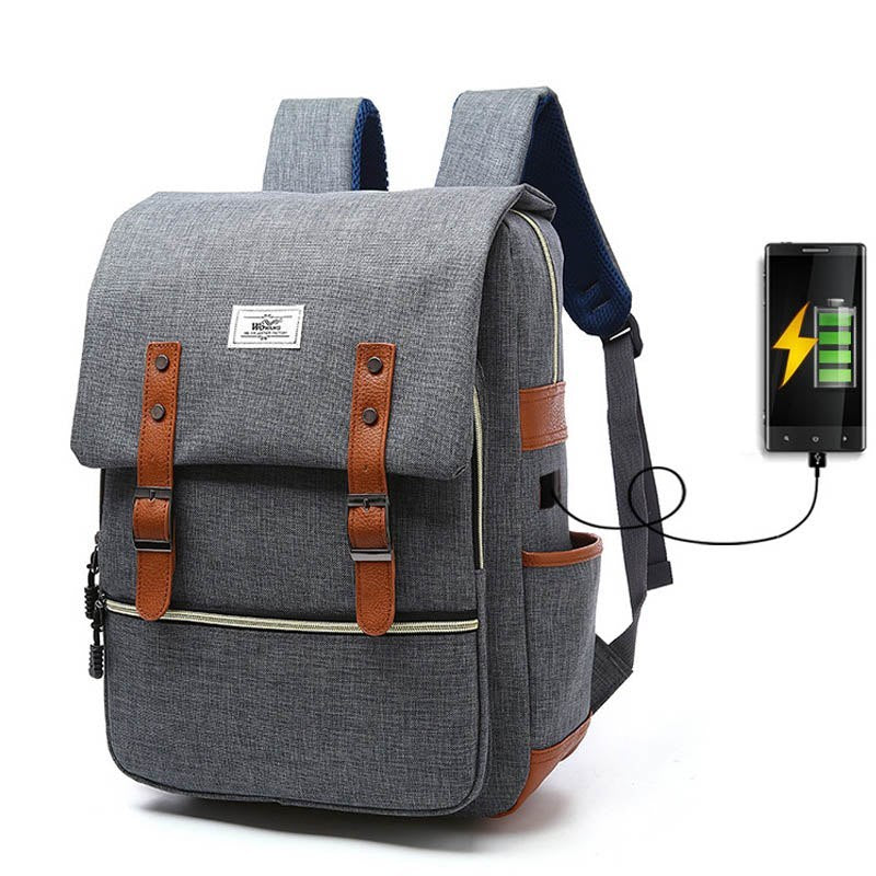 A gray canvas backpack with brown leather accents and a USB charging port, designed for men and women's school or travel use.