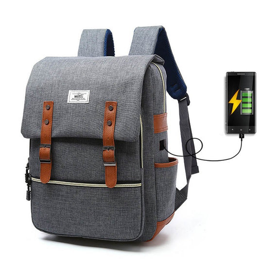 A gray canvas backpack with brown leather accents and a USB charging port, designed for men and women's school or travel use.