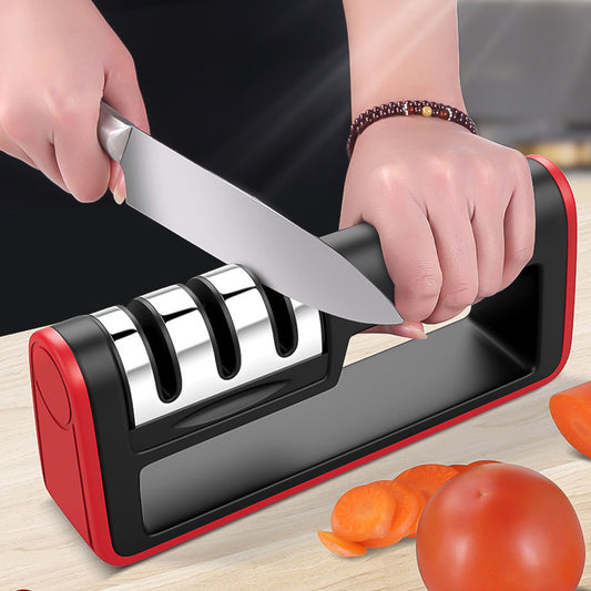 A hand using a professional knife sharpener with three sharpening stages on a kitchen countertop with sliced tomatoes nearby.