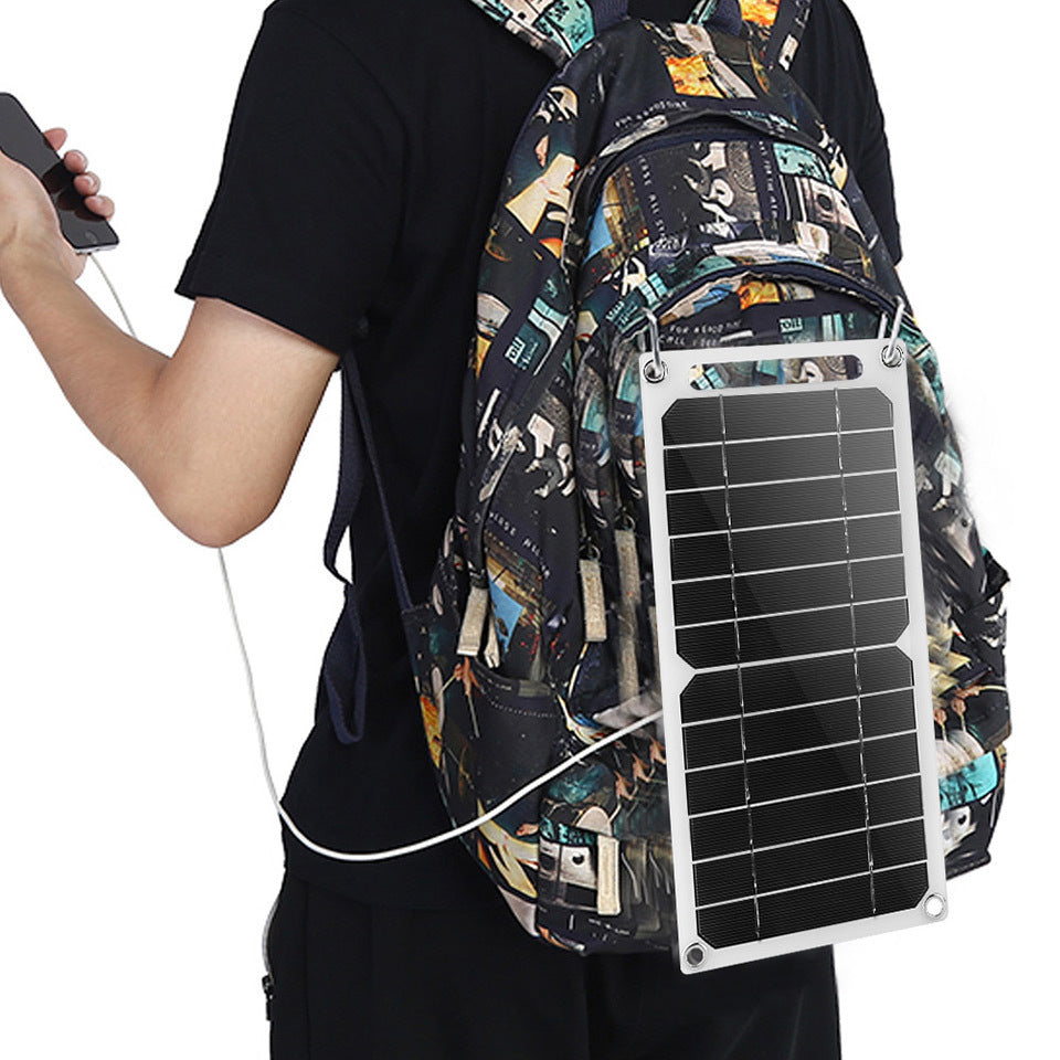 A person wearing a backpack with a solar panel attached to the back, holding a charging cable connected to a device.