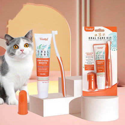 A presentation of pet oral care products including a toothbrush, finger toothbrush, and toothpaste with a cat looking on. The packaging features a white and orange color scheme and the brand is TropiClean.