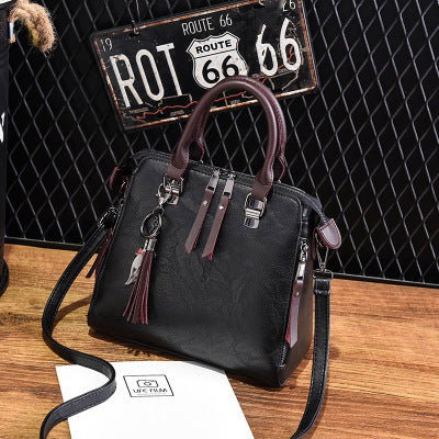 A black handbag with shoulder straps and a tassel detail, displayed in front of a sign that reads 'ROUTES 66'.