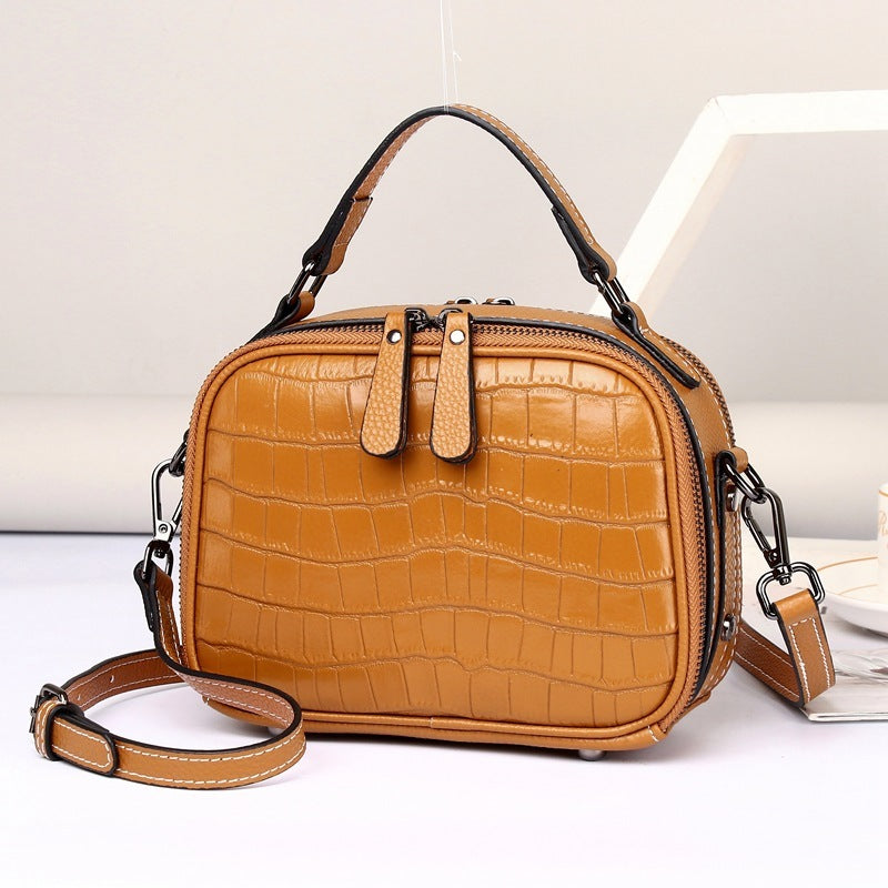 A brown crocodile patterned first layer cowhide crossbody handbag with a zipper opening and a shoulder strap.