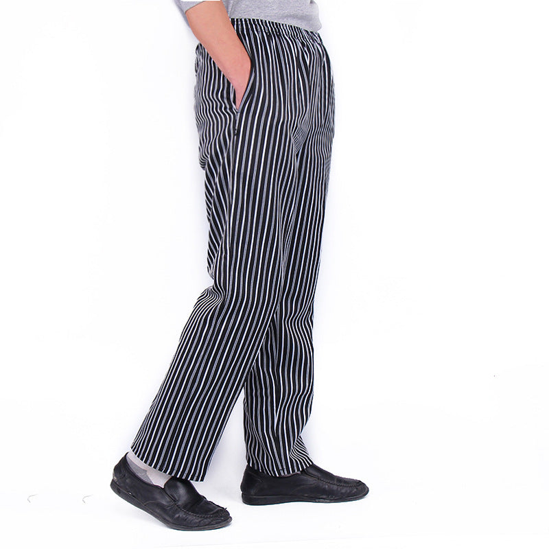 A person wearing black chef pants with white stripes, standing sideways and looking down.