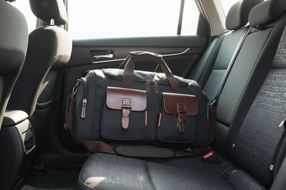 A black and brown canvas travel bag with leather accents and a shoulder strap.
