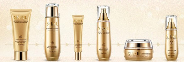 Collection of gold skincare products with clear packaging on a beige background.