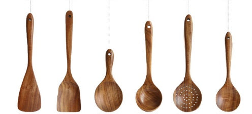 Set of wooden cooking utensils hanging against a white background
