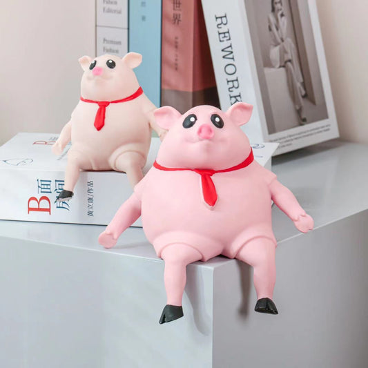 Two pink pig stress toys with red scarves, one larger than the other, sitting on a surface with books in the background.
