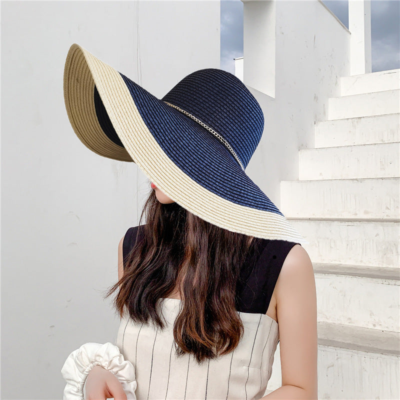 A woman wearing a navy blue and beige wide-brimmed straw hat with a flat top and a ribbon around the base.