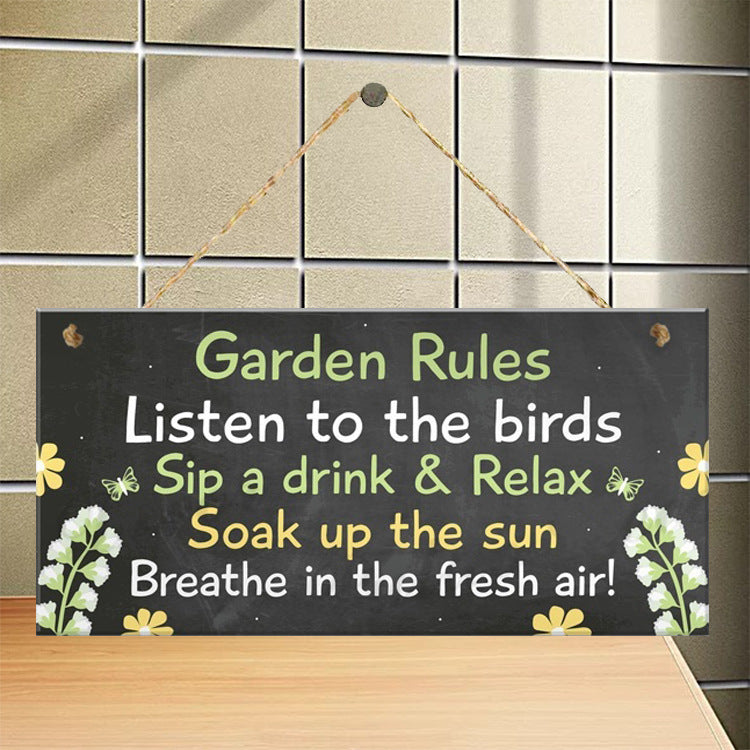 A wooden garden sign with black background and colorful text that reads 'Garden Rules Listen to the birds Sip a drink & Relax Soak up the sun Breathe in the fresh air!' with decorative flowers and butterflies.