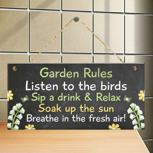 A wooden garden sign with black background and colorful text that reads 'Garden Rules Listen to the birds Sip a drink & Relax Soak up the sun Breathe in the fresh air!' with decorative flowers and butterflies.