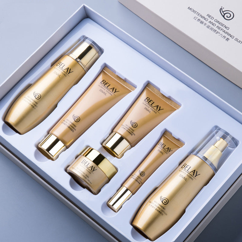 Skincare set with gold and beige bottles and tubes in a box.