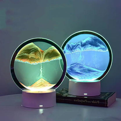 Two 3D Quicksand Table Lamps displaying different colors of quicksand within glass domes on circular white stands, placed on a flat surface with a book.