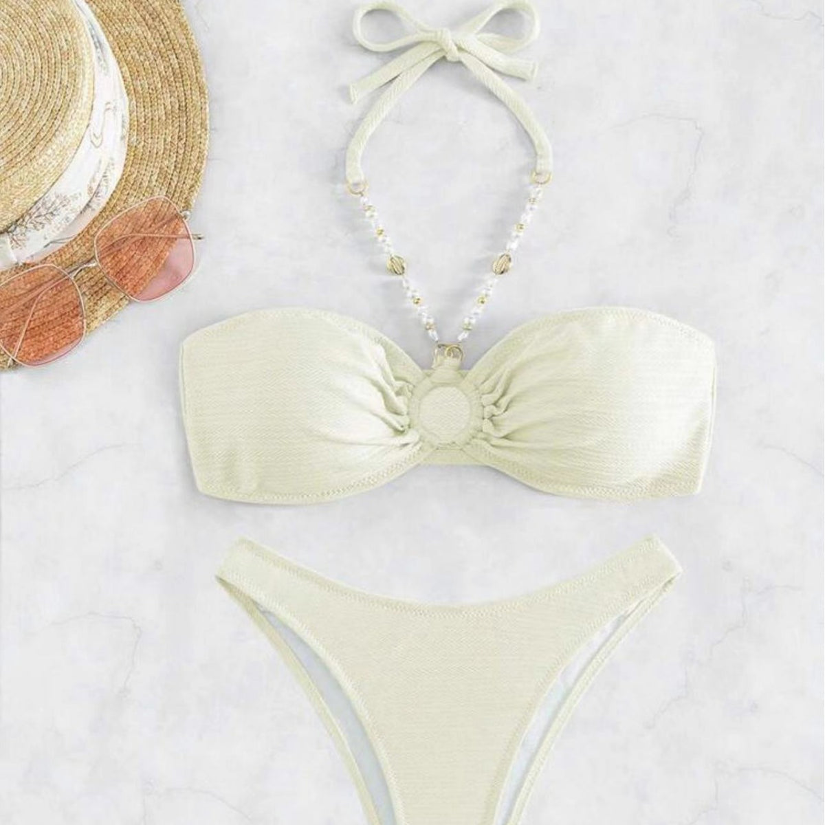 Light yellow bikini set on a marble surface with a straw hat and sunglasses.