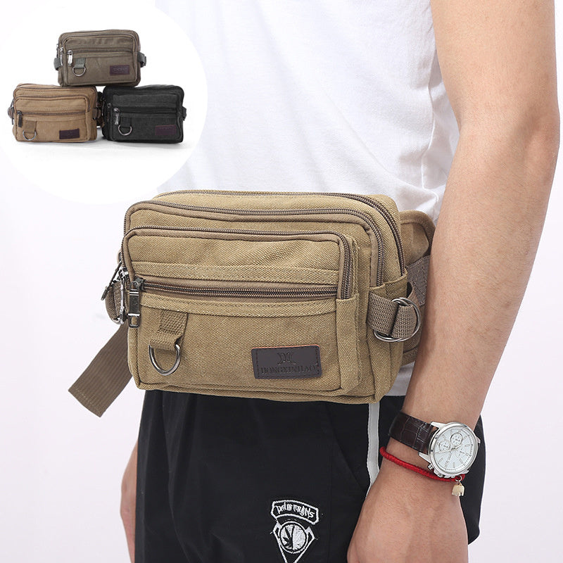 A person wearing a beige canvas fanny pack with multiple zipper pockets, designed for men's waist carrying.