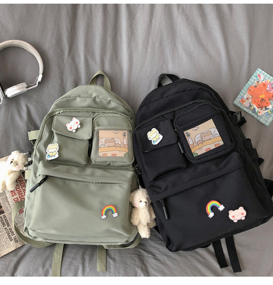 Two canvas backpacks, one green and one black, with a variety of accessories such as headphones, a teddy bear, and books scattered around them.