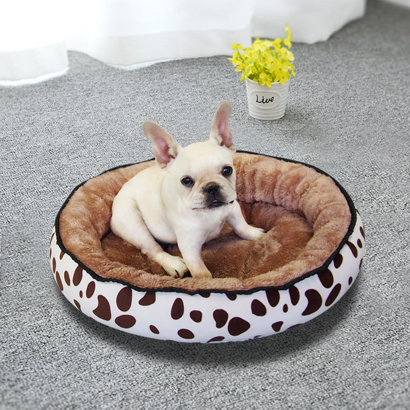 A small dog lying inside a round pet bed with a brown and white cow print design.