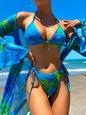 A woman wearing a blue and green floral bikini with a matching cover-up at the beach.