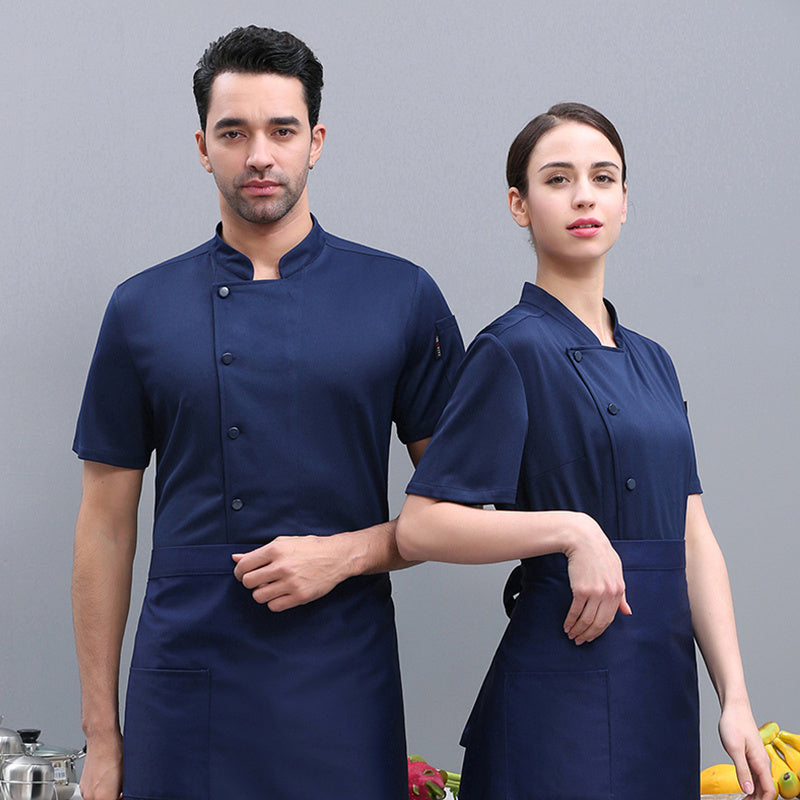 A male and a female model wearing navy blue short sleeve chef overalls, with the male model in front showing a three-quarter turn and the female model behind him showing a full face profile.