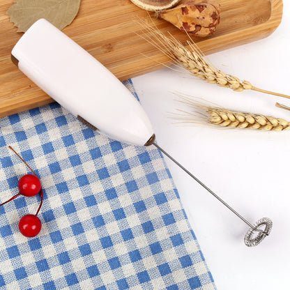An electric coffee blender egg beater in white color, pictured on a table with a blue and white checkered napkin, some cherries, and wheat ears.
