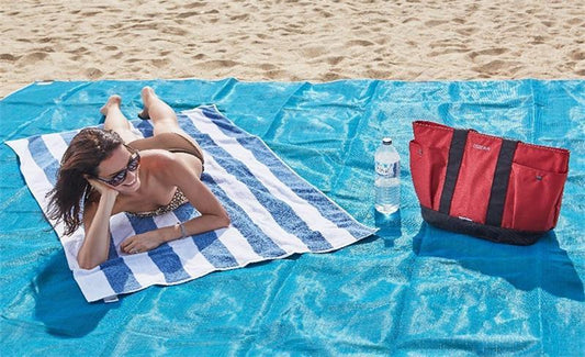 It's a blueish green beach mat. With a person laying on a towel on the mat on the beach sand.