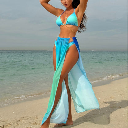 Woman in blue and green bikini and cover-up on a beach.