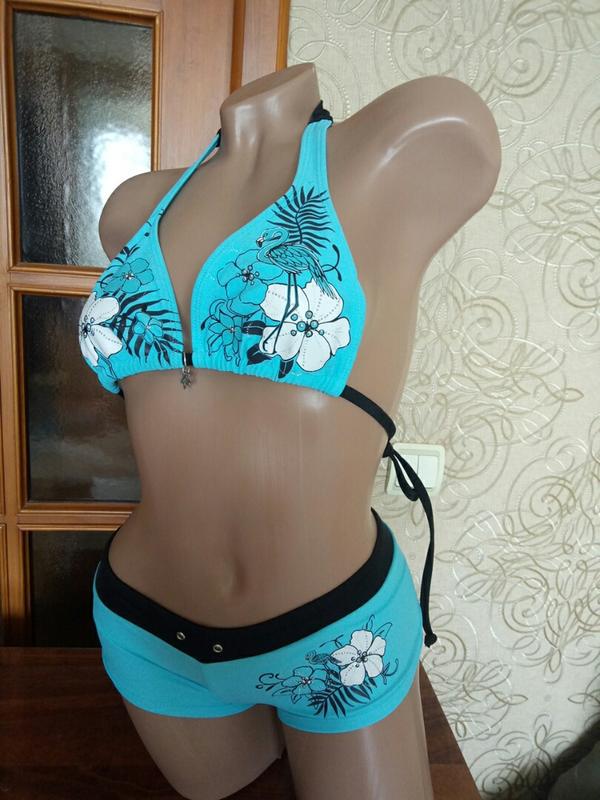 A bikini suit on a mannequin featuring a sky blue top with a floral pattern and a solid black bottom, set against a backdrop with various accessories and clothing items.