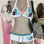A bikini suit on a mannequin featuring a sky blue top with a floral pattern and a solid black bottom, set against a backdrop with various accessories and clothing items.