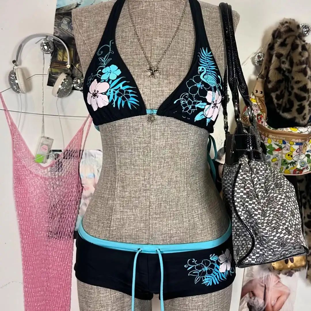 A bikini suit on a mannequin featuring a sky blue top with a floral pattern and a solid black bottom, set against a backdrop with various accessories and clothing items.