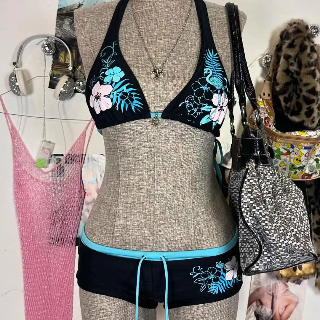 A bikini suit on a mannequin featuring a sky blue top with a floral pattern and a solid black bottom, set against a backdrop with various accessories and clothing items.